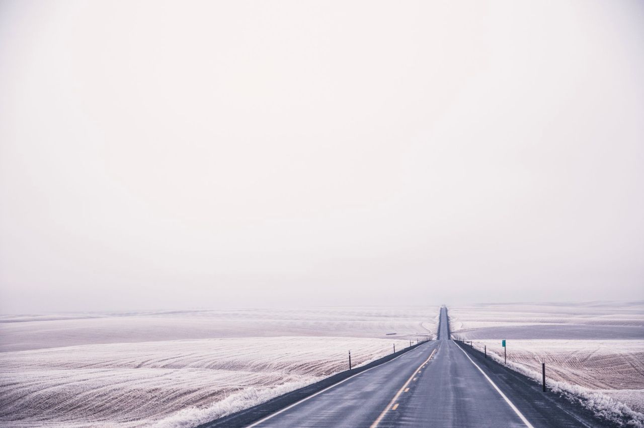 Route droite dans des champs enneigés sous un ciel blanc rosé